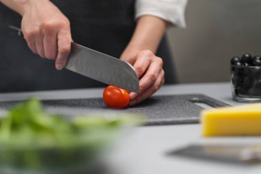 Beyaz üniformalı bir kadın şef ve restoran mutfağında siyah önlük. Aşçı büyük bir mutfak bıçağıyla sebzeleri keser..