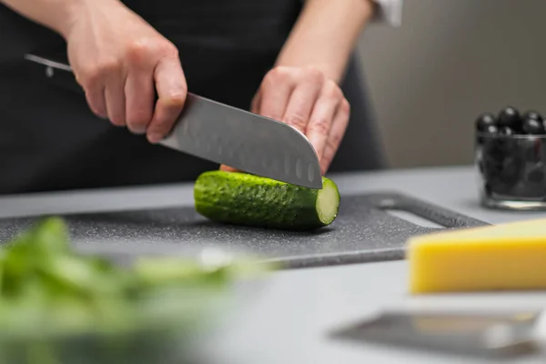 Una cuoca in uniforme bianca e un grembiule nero nella cucina del ristorante. Il cuoco taglia le verdure con un grande coltello da cucina. — Foto Stock