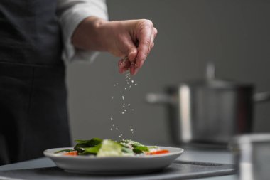 Beyaz üniformalı bir kadın şef ve restoran mutfağında siyah önlük. Aşçı salataya susam tohumu serper..