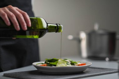 Beyaz üniformalı bir kadın şef ve restoran mutfağında siyah önlük. Yemek pişirmek. Aşçı yeşil bir şişeden zeytinyağı döker..