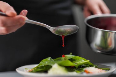 Beyaz üniformalı bir kadın şef ve restoran mutfağında siyah önlük. Aşçı kırmızı kızılcık salatası sosu döker. Yemek yapmak ve dekore etmek..