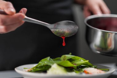 Beyaz üniformalı bir kadın şef ve restoran mutfağında siyah önlük. Aşçı kırmızı kızılcık salatası sosu döker. Yemek yapmak ve dekore etmek..