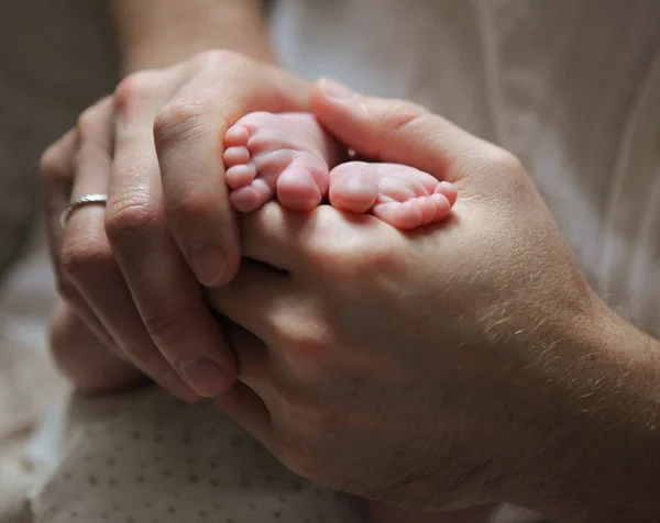 Las manos de los hombres sosteniendo los pies del bebé recién nacido —  Fotos de Stock