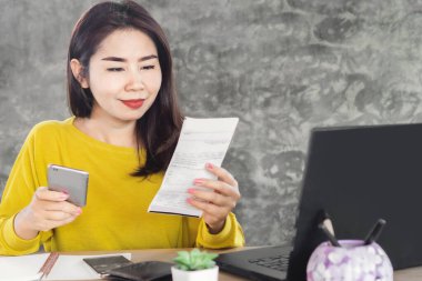Elektrik faturasını akıllı telefonla ödeyen mutlu Asyalı kadın.