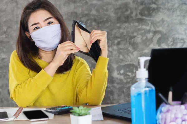 sad Asian woman wearing protective mask hand open empty purse having financial problem during self-quarantine from covid-19 virus pandemic