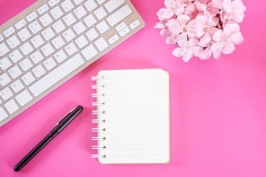 çiçek, klavye, kalem ve not defteri pembe arka planda yatıyordu