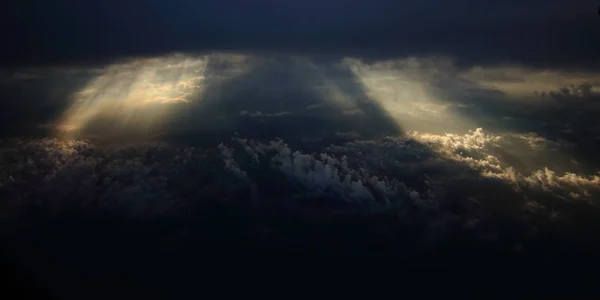 Lichtstrahlen, die durch dunkle Wolken auf einer anderen Wolkenschicht für den Hintergrund scheinen — Stockfoto