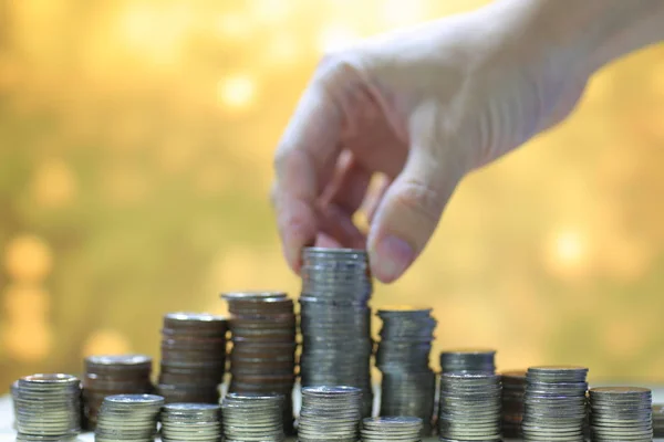 Munt stapel rij hand met munt maken een toren. Geel gouden circulaire lichte achtergrond. — Stockfoto