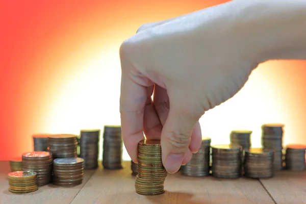 Coin piles and hand holding coin making a coin stack towerhandling coin making a coin stack columnnon-order coin piles with blurred background. Business savings financial concepts on wooden table.