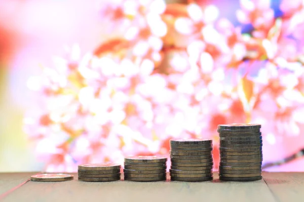 Environmental friendly economy. Finance business of saving nature. Coin pile stacked in increasing chart shape on wood board with out of focus pink flower background.