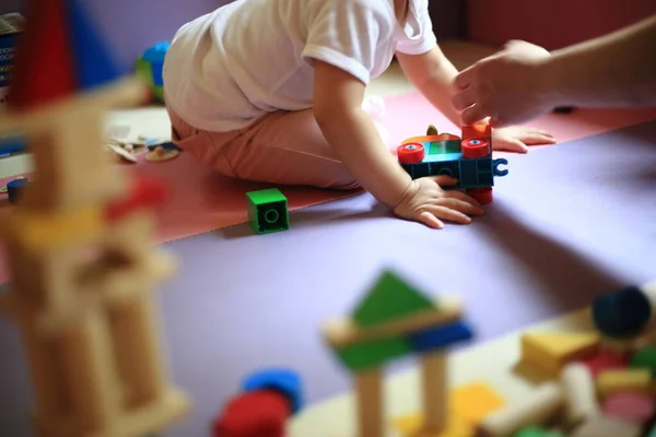 blurred baby playing toy block in the background. selective focus on castle made of colorful wooden blocks. baby learning by playing. brain and muscle development in young and infant stage.