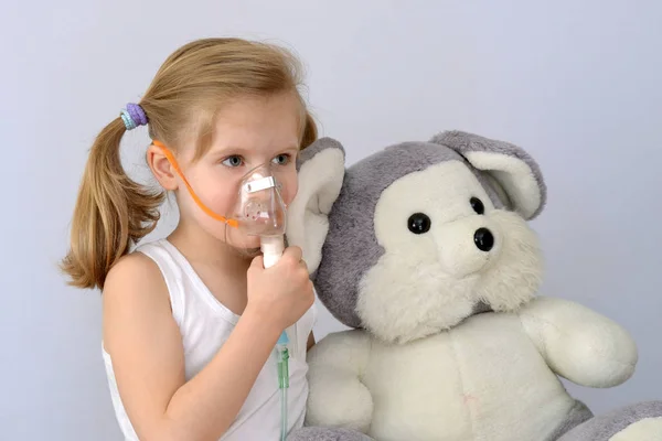 Niño (niña) con un inhalador (nebulizador) hace que el procedimiento sea un juguete suave . — Foto de Stock