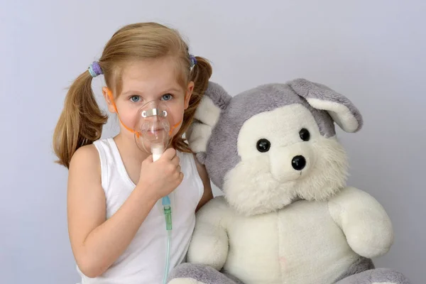 Niño (niña) con un inhalador (nebulizador) hace que el procedimiento sea un juguete suave . — Foto de Stock