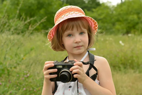Portrait of a baby photographer (a little girl) with a camera on the background of nature. — Stock Photo, Image