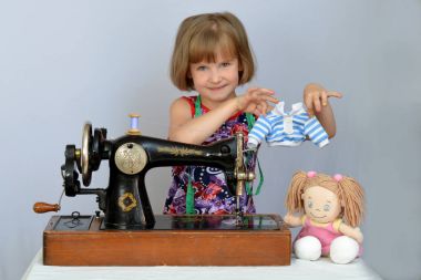 child, kid,(little girl) seamstress sews clothes for the dolls on the old sewing machine. clipart