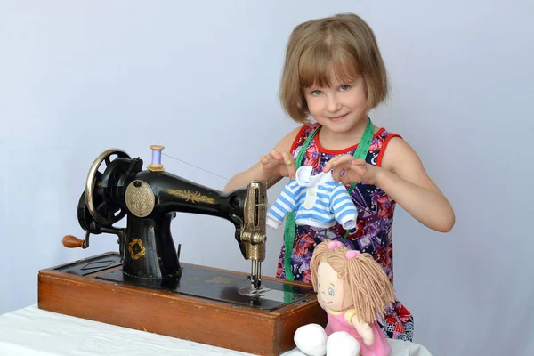 child, kid,(little girl) seamstress sews clothes for the dolls on the old sewing machine.