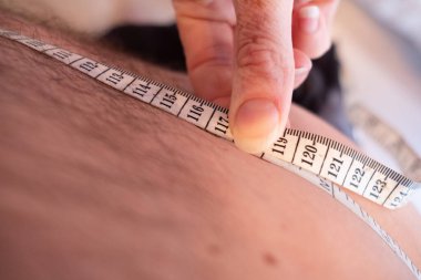 Kıllı bir erkeğin midesini kapatırken vücudunun yağ hesaplamalarının bir parçası olarak belinin ölçüsünü alıyor.