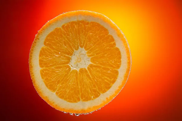 Rebanada de naranja fresca en agua con burbujas en la parte posterior del gradiente naranja — Foto de Stock