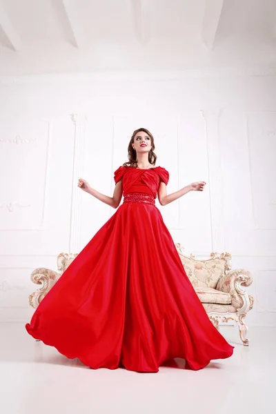 Mujer elegante en un vestido largo rojo está de pie en una habitación blanca, d —  Fotos de Stock