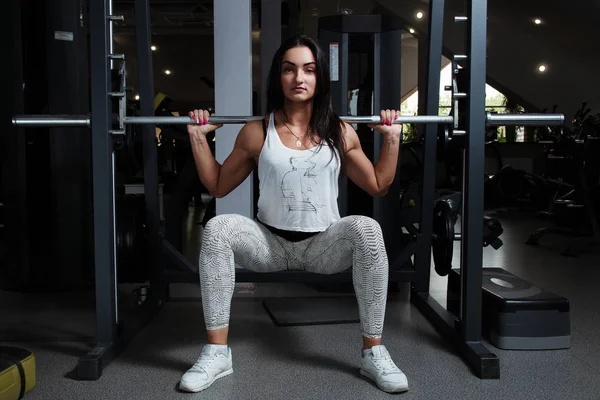 Chica joven con la figura inflada sexual, en el gimnasio, sentadillas con —  Fotos de Stock