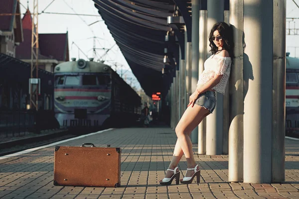 Osamělá mladá bruneta žena s starý kufr stojí na nástupišti stanice — Stock fotografie
