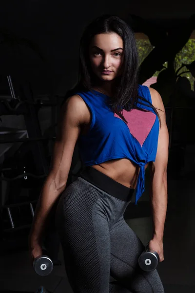 Young girl with sexual inflated figure, standing in the gym holding a dumbbell — Stock Photo, Image