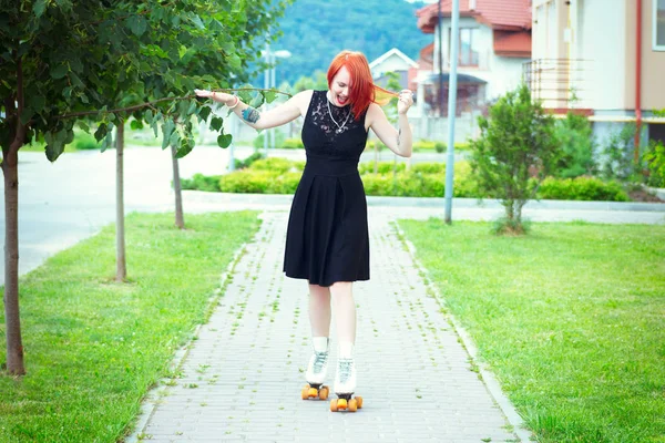 Rudowłosa dziewczyna w czarnej sukni w Wrotki na chodniku — Zdjęcie stockowe