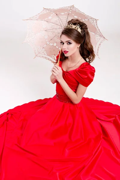 Elegant woman in a long red dress sitting on the floor and holding a vintage umbrella