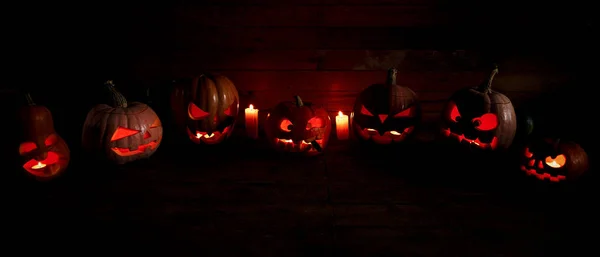 O conceito de Halloween. Muitas abóboras assustadoras zangadas de luz ardente brilhante. jack lanterna no escuro, em um fundo de madeira — Fotografia de Stock