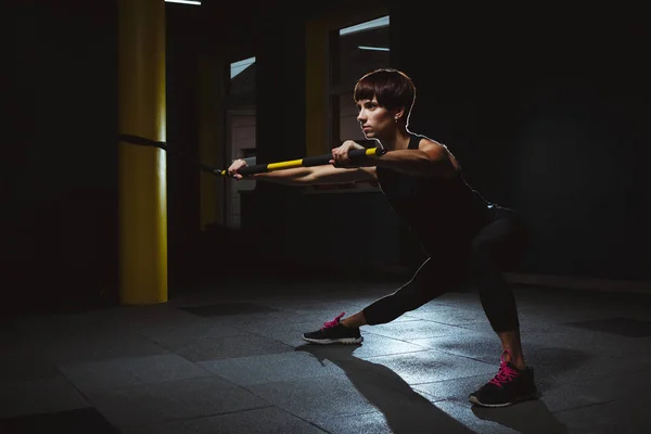 Fitness girl facendo esercizi di crossfit in palestra con trx in dark ha — Foto Stock