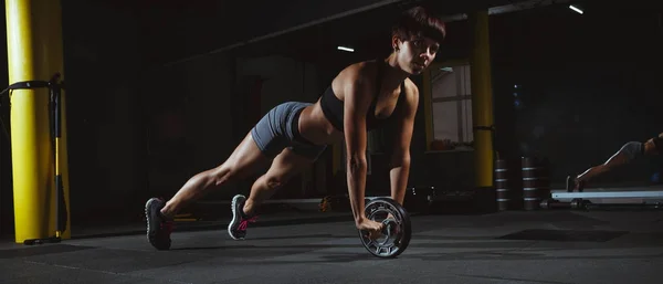 Fitness lány csinál crossfit gyakorlatok edzőteremben kerék sötétben — Stock Fotó