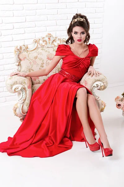 Elegante donna in abito rosso lungo seduta su sedia vintage in cui — Foto Stock