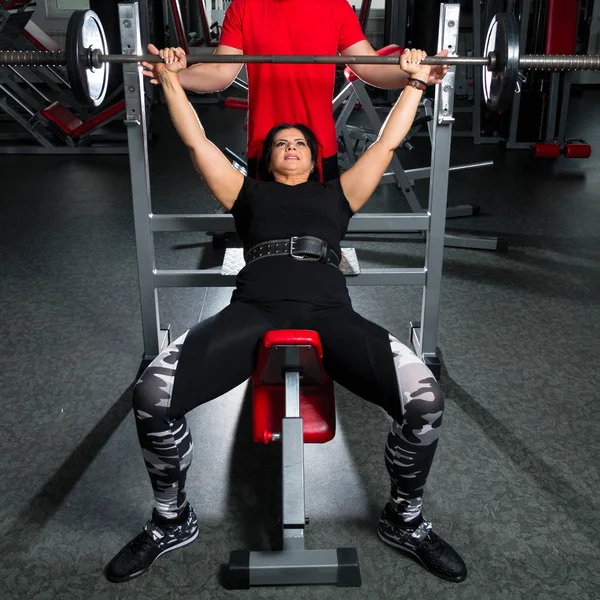 Mujer más tamaño en el gimnasio haciendo ejercicios con barra de levantamiento de pesas, f —  Fotos de Stock