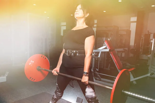 Mulher plus size no ginásio fazendo exercícios com powerlift barbell, f — Fotografia de Stock