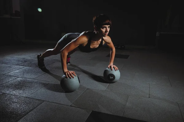 Chica de fitness haciendo ejercicios en el gimnasio con bolas en el pasillo oscuro, spo —  Fotos de Stock