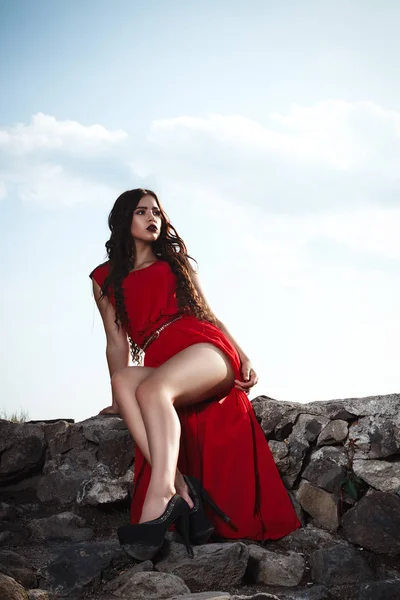 Сексуальная девушка в красном платье позирует на старом скальном замке с длинными ногами — стоковое фото