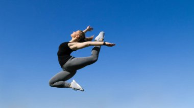 Genç güzel sarışın spor kız mavi gökyüzü backg üzerinde atlama