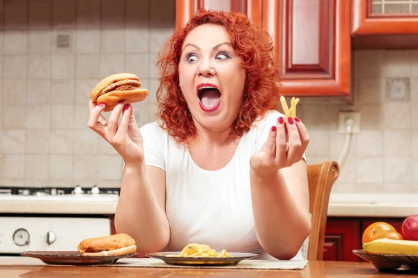 Grote vrouw eten fastfood. De dik meisje rood haar met Hamburger, aardappel een — Stockfoto