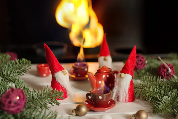 Ajutoarele lui Moș Crăciun stau lângă șemineu cu decorațiuni de Crăciun și beau ceai fierbinte. Craciun coada . — Fotografie, imagine de stoc
