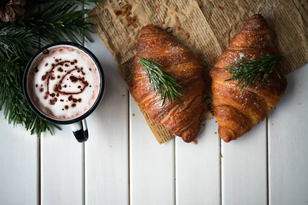 Frische und leckere Croissants auf einem weißen Holztisch mit einer Tasse Kakao oder Kaffee. — Stockfoto