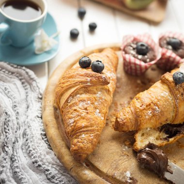 Taze kruvasanlar, meyve, kahve, kek ve çikolata yapıştırma üzerinde beyaz ahşap masa ile Kahvaltı.