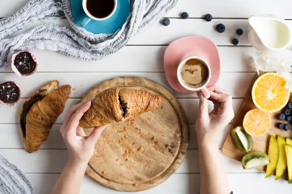 Młoda kobieta ma pyszne śniadanie obejmujące kawę, rogaliki, babeczki i owoce na biały drewniany stół — Zdjęcie stockowe