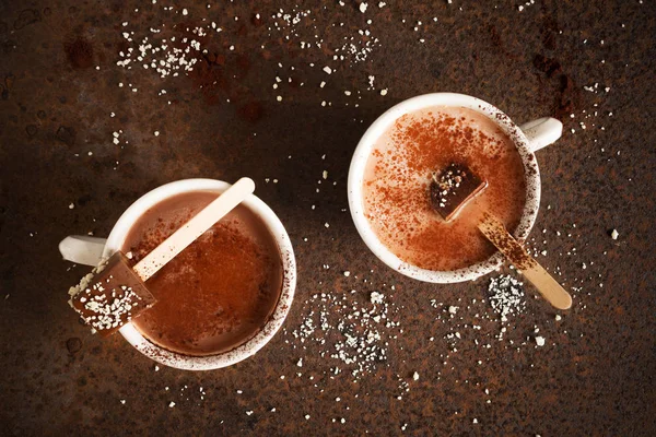 Two cups of hot chocolate with cocoa powder Chocolate on stick Top view