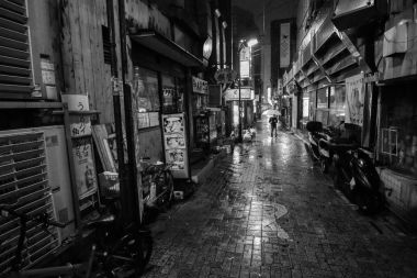 Siyah ve beyaz bir adamın yalnız bir alleyway yağmurlu bir gecede Tokyo şehirde yürüyüş bir şemsiye ile