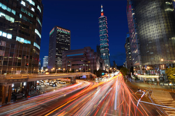 Red light trails from vehicle traffic streak across a busy intersection in front of Taipei 101