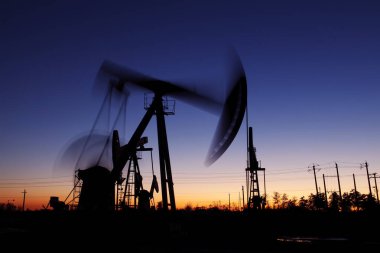 Petrol sahası sahnesi, ışın pompalama ünitesinin siluette olduğu gece. 