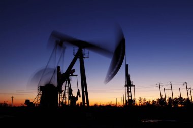 Petrol sahası sahnesi, ışın pompalama ünitesinin siluette olduğu gece. 