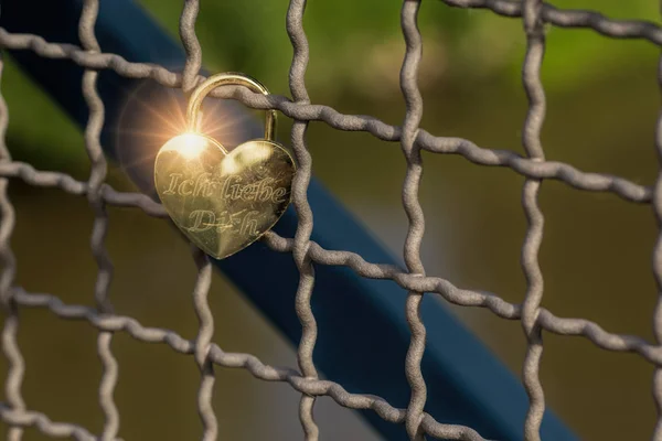 Heart shaped love padlock attatched to wire fence on a bridge. T — Stock Photo, Image