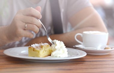 Parça kremalı tatlı pasta bir çatal ile bir adamın elini kesti. Ahşap bir masa üzerinde kahve.