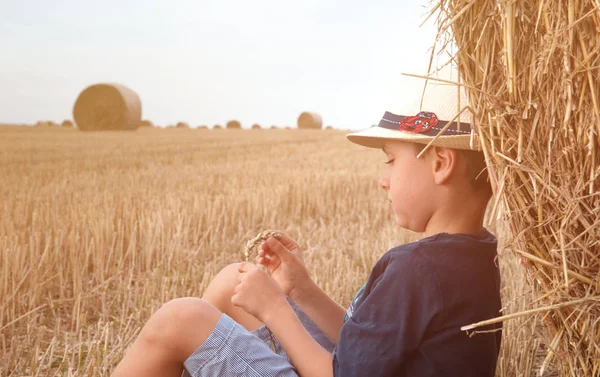 Joven chico de campo lindo en sombrero cerca de pajar al atardecer en verano. Concepto de verano, unas vacaciones.Activo ocio al aire libre con los niños en el cálido día de verano . —  Fotos de Stock